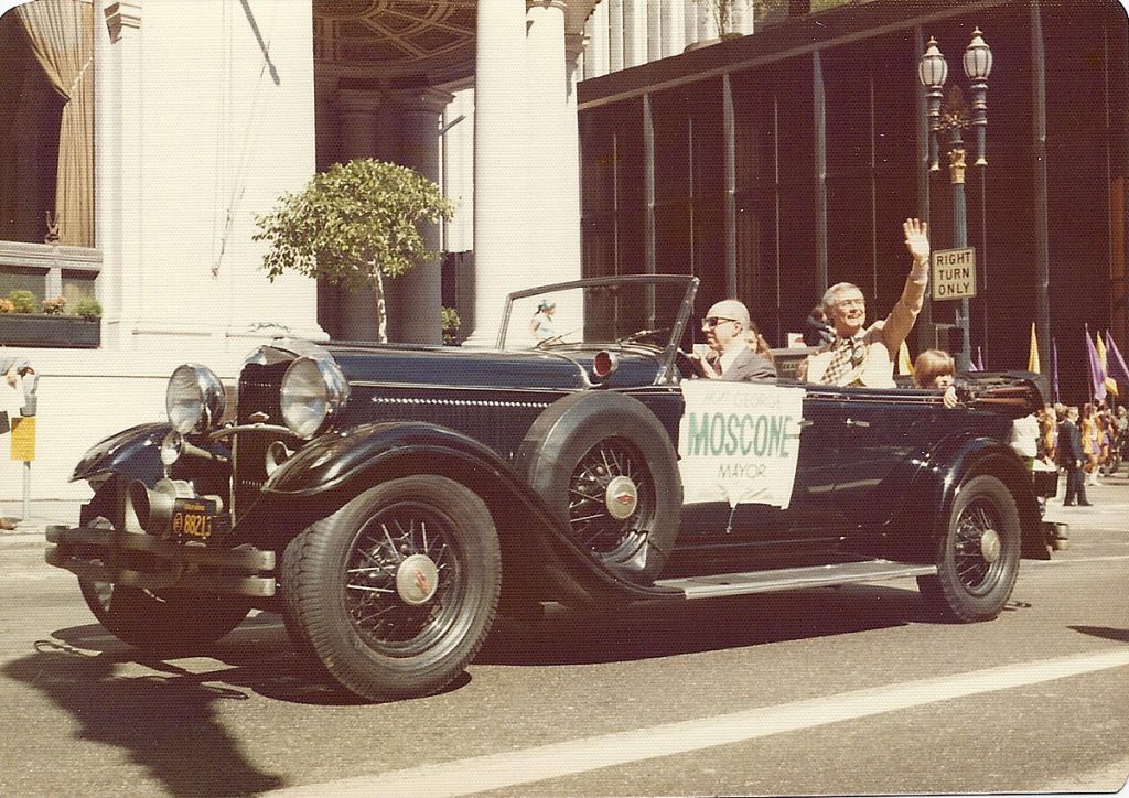 George Moscone waving from a car