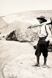 Annie Alexander with pick axe over her shoulder in rocky, mountainous terrain