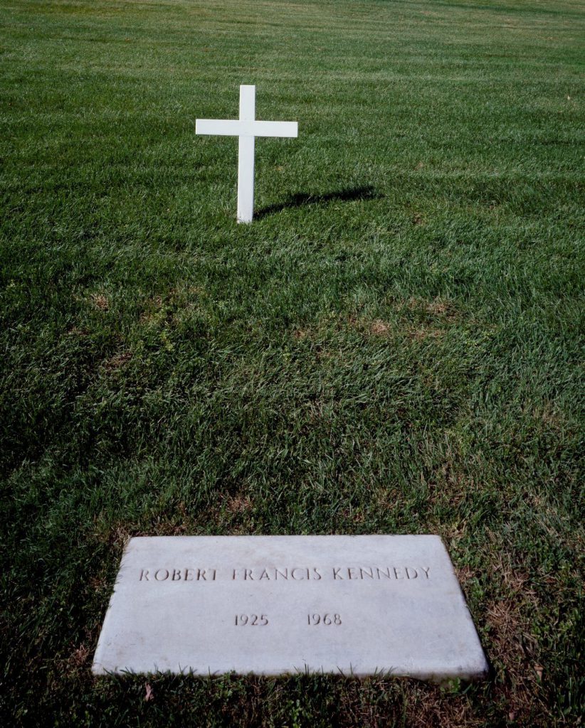 Shows a gravestone in grass bearing the name Robert Francis Kennedy, a cross in the background