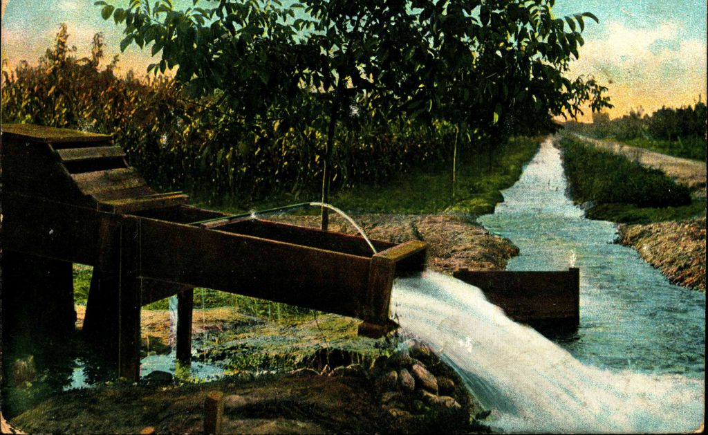 Water pours from a metal structure to help irrigate orchard seen in the background.