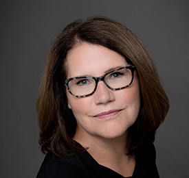 A woman with a brown bob and glasses smiles into the camera.