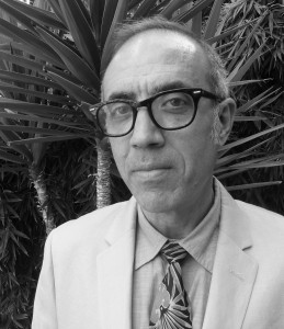 A black and white photo of a man with a serious expression on his face, wearing a suit and black frame glasses.